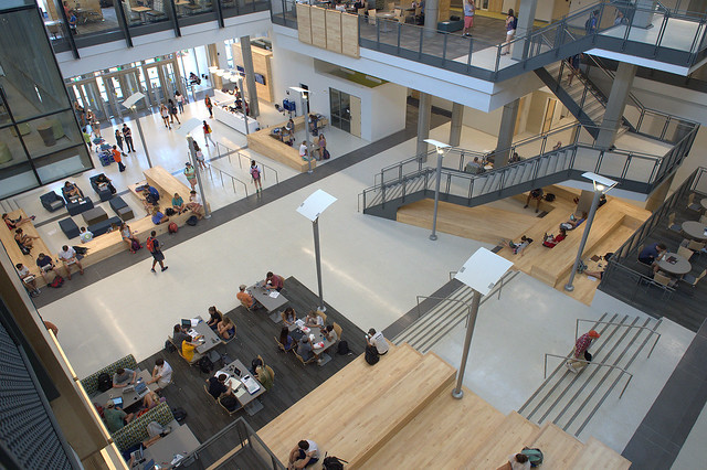 An overhead photo shows the atrium of the Mell Classroom Building, with the entrance to the building at the top of the photo and the staircase to the left.