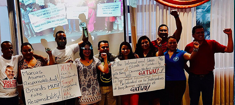 Union League members in the Americas hold signs supporting GATWU in Bangalore, India, where workers are being targeted for organizing, calling on brands to take responsibility!