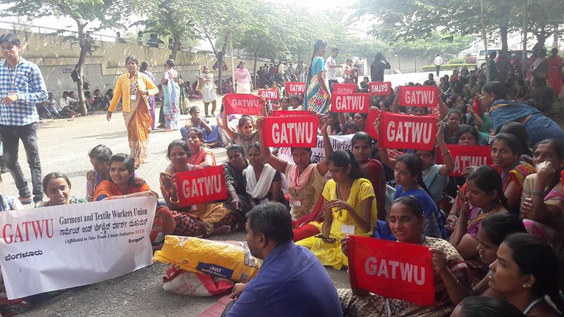 Women garment workers protest the closing of their Shahi Exports factory outside, holding signs reading "GATWU" or "Garment and Textile Workers' Union" in Bangalore, India