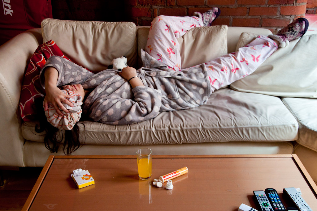 Woman in nightgown lying on the couch with a bag of ice on her head.
