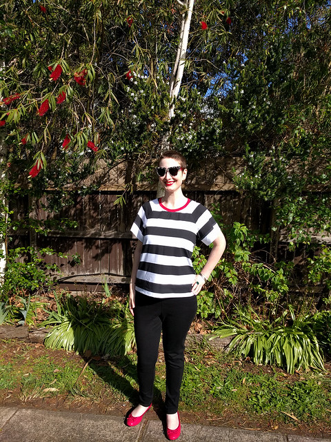 A woman poses in a garden, wearing a black and white striped tee and black ponte pants.