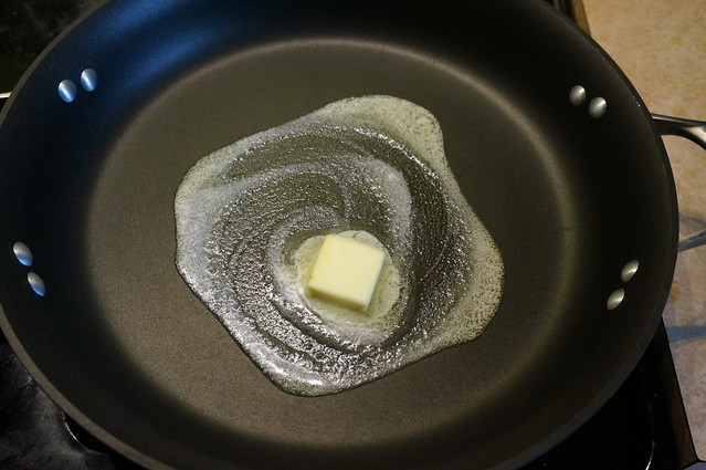 A swirl of butter in a nonstick pan, the pale yellow pat standing out against the black surface, buffered by a blanket of tiny bubbles