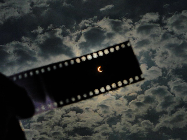 An image of individual holding up camera film to view a solar eclipse. 