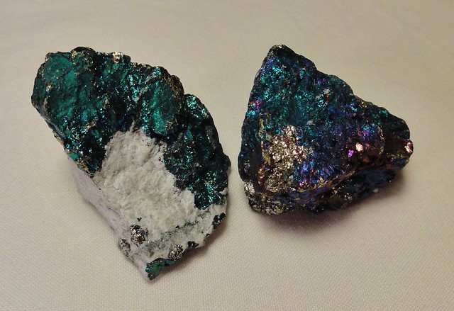 Image shows two pieces of boronite, a copper mineral that is an irridescent mix of blues, blue-greens, purples, magentas, and golds.