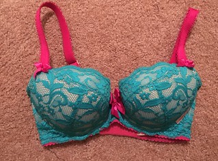 The base color for the bra is beige, and the lace is a dark turquoise green with pink accent pieces.
