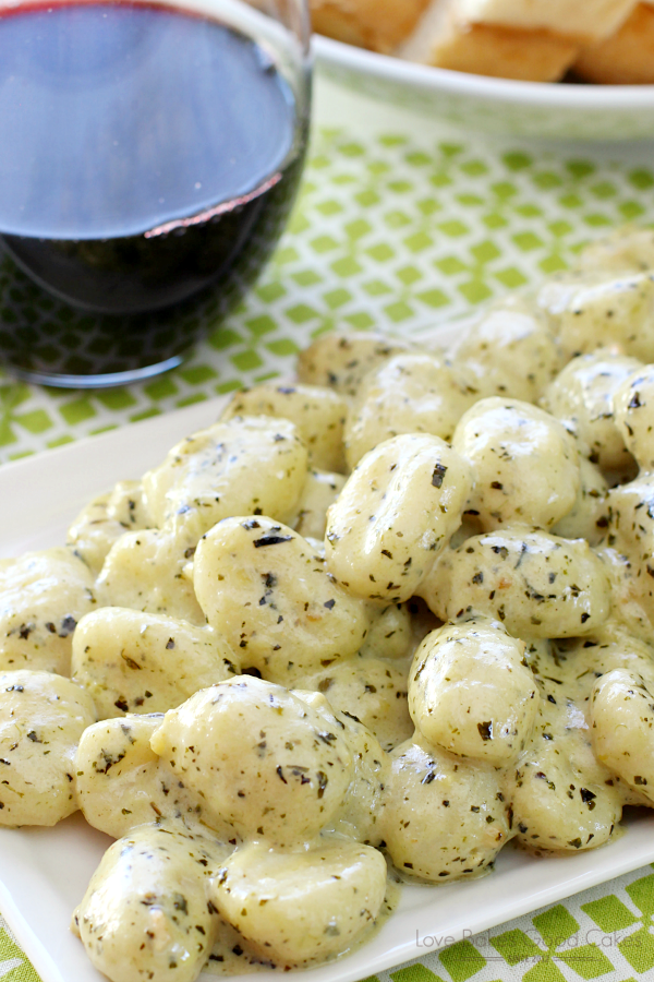Gnocchi with Pesto Cream piled up on a white plate with a glass of red wine.