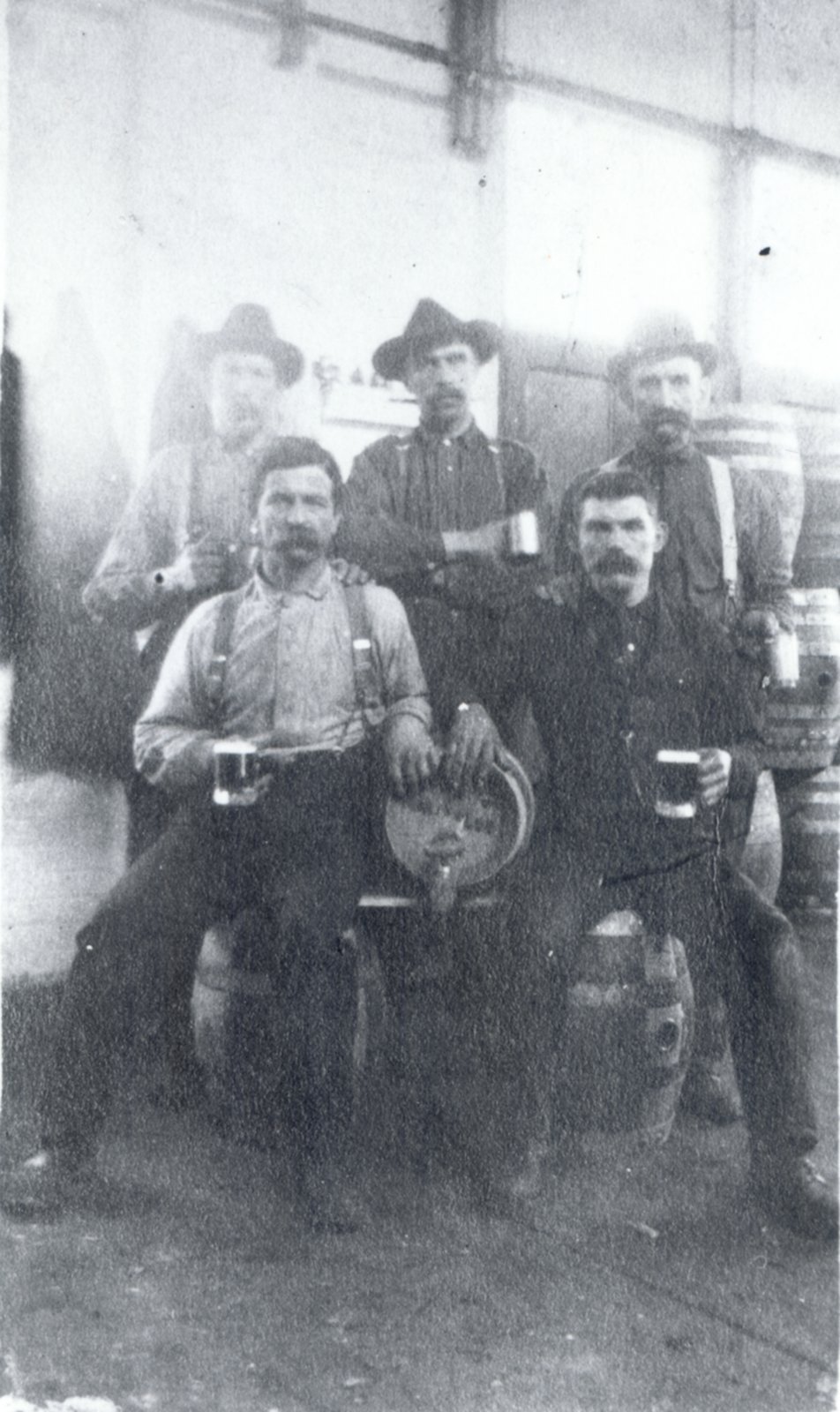 Men sitting with kegs, holding glasses of beer