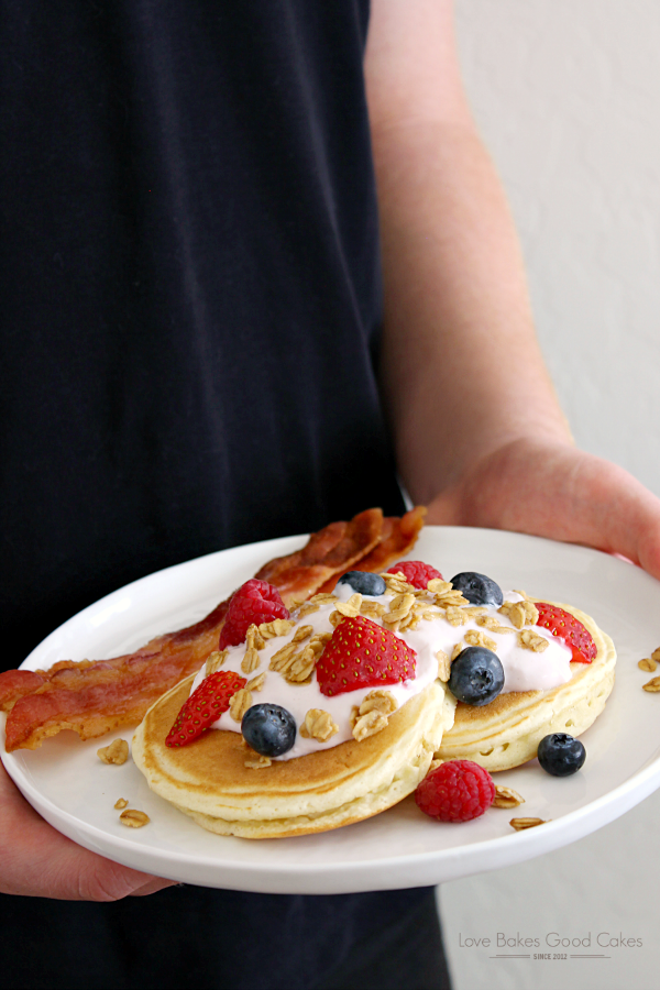 A plate of pancakes with bacon and fresh berries in someone's hands.