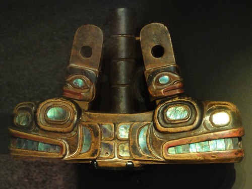 Image shows a wooden pipe of stylized killer whale heads back-to-back, inlaid with abalone shell.