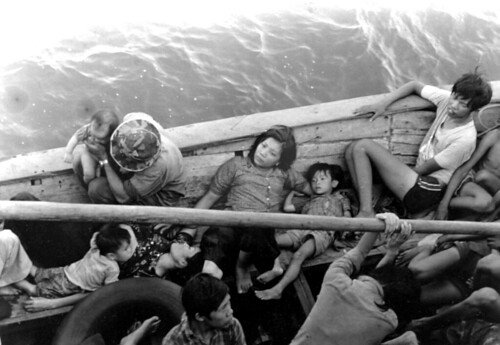 Vietnamese refugees rest in their boat, as the guided missile cruiser USS FOX (CG-33) (not visible) comes alongside