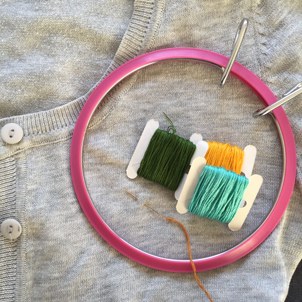 grey cardigan with several skeins of embroidery floss and an embroidery hoop