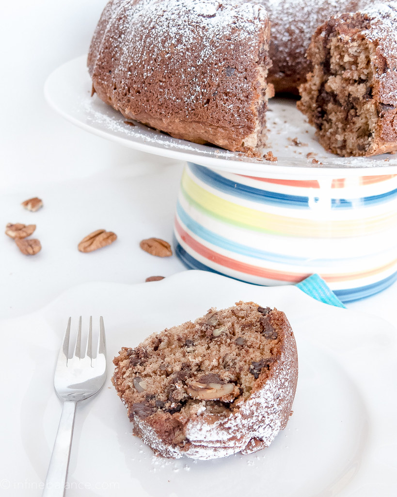 chocolate chip bundt cake with pecans, sliced on a cake with whole cake in background
