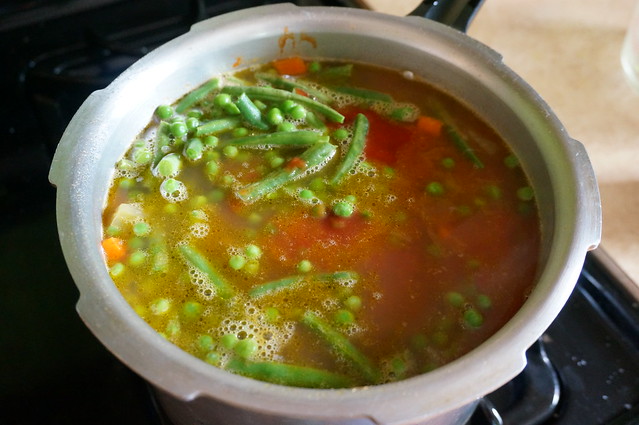 Peas and green beans float on top of beans and broth in a pressure cooker, not yet mixed in.