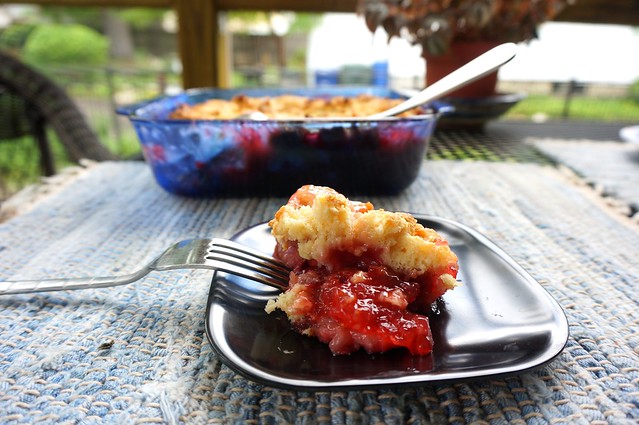 A scoop of strawberry cobbler, bright red filling against a small black plate, with a fork resting, tines down, on the edge of the plate